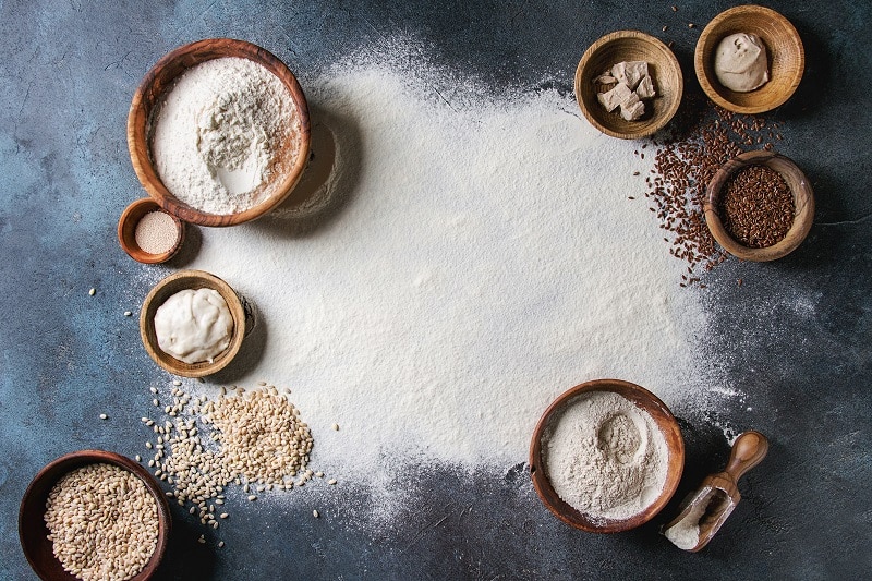 Ingredients for baking bread. Variety of wheat and rye flour, grains, yeast, sourdough and sifted flour over dark blue texture background. Flat lay, space